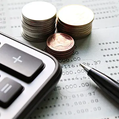 A paper, a calculator, a pen and stacks of coin on a table.