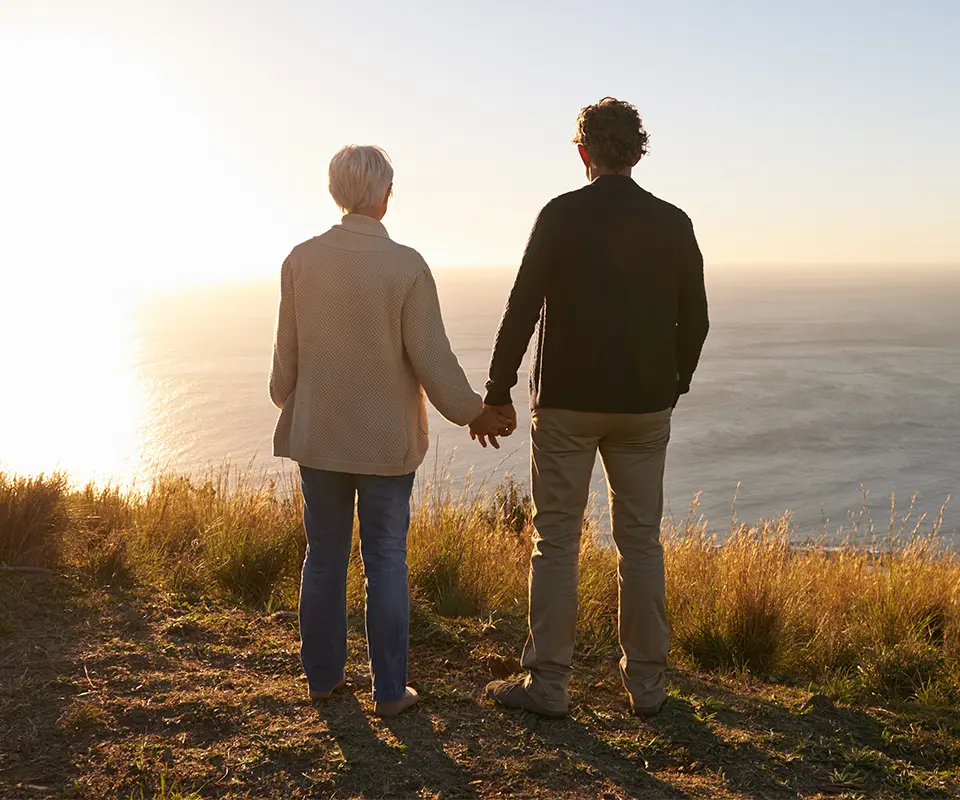 A man and a woman holding hands and watching a sunset.